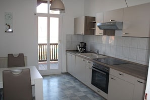 A modern kitchen with a built-in oven, a coffee maker, and a window overlooking a wooden deck. - Holiday apartment with 1 bedroom (Wernigerode)