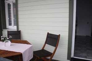 An outdoor seating area with a table and chairs, a window, and a view of a dark interior space. - Holiday apartment with 1 bedroom (Wernigerode)