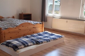 A bedroom with a wooden bed, a bedside table, a radiator, and a window with curtains. - Holiday apartment with 1 bedroom (Wernigerode)