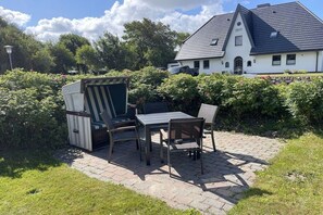 A patio with outdoor furniture, a white house with a dark roof in the background, and a hedge in the foreground. - Holiday apartment with 3 bedrooms (Morsum)