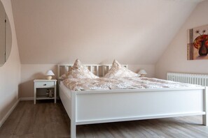 A bedroom with a white bed, two bedside tables with lamps, a radiator, and a painting on the wall. - Siewertsen Apt. No. 1 (Alkersum)