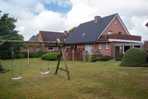 A residential property with a brick house, a swing set, and a well-maintained lawn. - Siewertsen Apt. No. 1 (Alkersum)