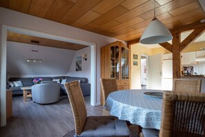 A modern interior with a dining area, a sofa, and a kitchen visible through an open door. - Siewertsen Apt. No. 1 (Alkersum)