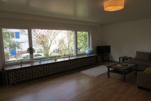 Ein Wohnzimmer mit großem Fenster, einer Couch, einem Couchtisch und einem Fernseher.