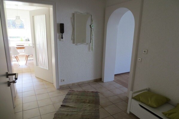 Ein Flur mit Fliesenboden, einer Tür zum Balkon, einem Spiegel an der Wand und einer Bank mit Kissen.