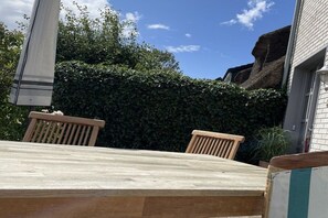 A wooden table with two chairs, a hedge, and a building in the background. - Holiday home with 2 bedrooms (Nordstrand)