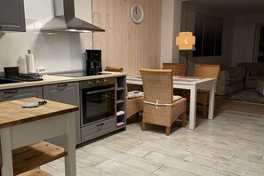 A compact kitchen with a stove, oven, and a dining area with wicker chairs and a table. - Holiday home with 2 bedrooms (Nordstrand)