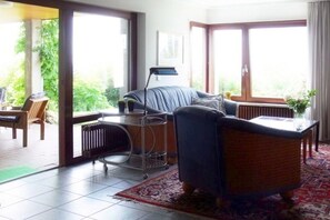 A living room with a sofa, a small table, and a radiator. There is a window with a view of greenery outside. - Holiday apartment with 1 bedroom (Bad Bellingen-Bamlach)