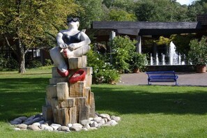 A sculpture of a seated figure with a red shoe, surrounded by rocks, in a park with a fountain and a bench. - Holiday apartment with 1 bedroom (Bad Bellingen-Bamlach)