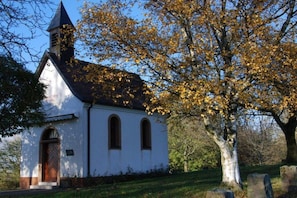 A church with a white facade, a pointed steeple, and a large tree with autumn leaves in the foreground. - Holiday apartment with 1 bedroom (Bad Bellingen-Bamlach)