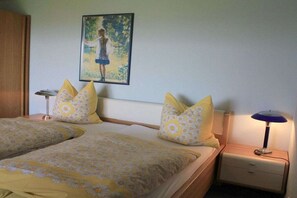 Une chambre avec deux lits, chacun agrémenté d’une literie à motifs floraux, une table de chevet avec une lampe et un tableau au mur.