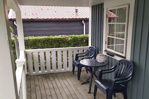 A covered porch with a table and chairs, a window, and a view of a building with a red roof. - Holiday home in Steendam with swimming pool (Steendam)