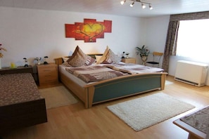 Ein Schlafzimmer mit Bett, Nachttischen, einem Fenster mit Vorhängen und einem an der Wand hängenden Kunstwerk.