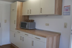 Een kitchenette met witte kastjes, een magnetron en een houten aanrecht.