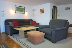 Ein Wohnzimmer mit einer Couch, einem Sessel, einem Hocker und einem Couchtisch.