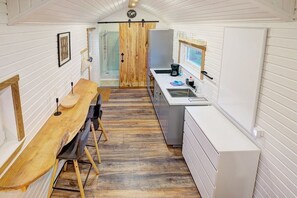 A compact kitchen with a wooden dining table, a refrigerator, and a window. - Holiday home with 1 bedroom (Westerdeichstrich)