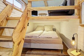 A loft-style bedroom with a bunk bed, a bedside table, a lamp, and a window. - Holiday home with 1 bedroom (Westerdeichstrich)