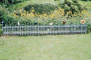A garden with a white picket fence, various plants, and yellow flowers. - Holiday apartment with 1 bedroom (Zwiesel)