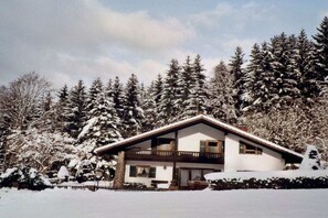 A two-story chalet with a balcony, surrounded by snow-covered trees. - Holiday apartment with 1 bedroom (Zwiesel)