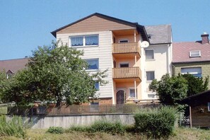 Un edificio residenziale a più piani con balconi, un'antenna parabolica e un cortile recintato.