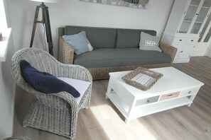 A room with a wicker chair, a white sofa, and a white coffee table. - Holiday apartment in Krummhörn with Wi-Fi (Krummhörn)