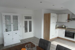A modern kitchen with white cabinetry, a dining table with chairs, and a built-in oven. - Holiday apartment in Krummhörn with Wi-Fi (Krummhörn)