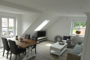 A modern living space with a dining area, seating, a TV, and a view through a window. - Holiday apartment in Krummhörn with Wi-Fi (Krummhörn)