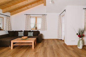 A cozy living room with a wooden ceiling, a dark brown sofa with patterned cushions, a wooden coffee table, and a vase with flowers on a white wall. - House at Kramer Holiday Apartment Kramer (Garmisch-Partenkirchen)