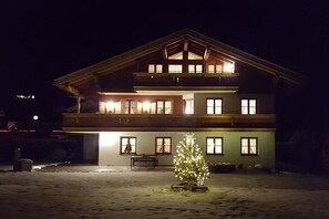 A two-story building with a balcony, a lit Christmas tree, and a bench outside. - House at Kramer Holiday Apartment Kramer (Garmisch-Partenkirchen)