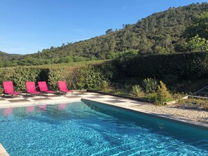 Une piscine d’un bleu éclatant, agrémentée de quatre chaises longues rouges et d’une terrasse à motifs à carreaux.