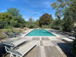 A rectangular swimming pool with a wooden deck and lounge chairs.