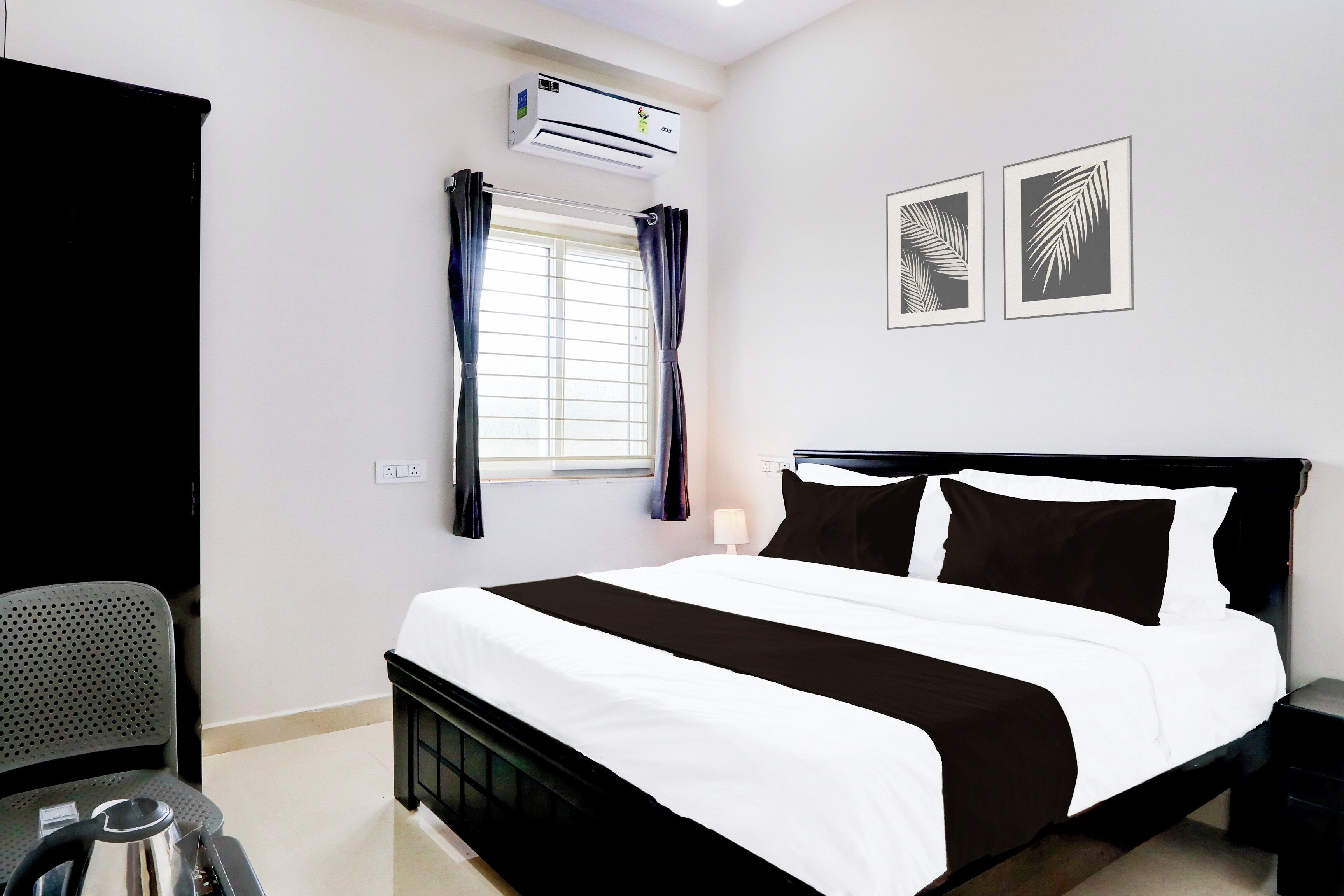 A hotel room with a bed, a desk, an air conditioner, a window with curtains, and two wall-mounted pictures.