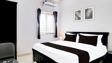 A hotel room with a bed, a desk, an air conditioner, a window with curtains, and two wall-mounted pictures.