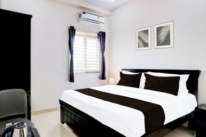A hotel room with a bed, a desk, an air conditioner, a window with curtains, and two wall-mounted pictures.