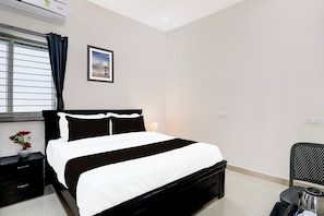 Quarto de hotel com cama, mesa de cabeceira, abajur, cadeira e janela com cortinas.