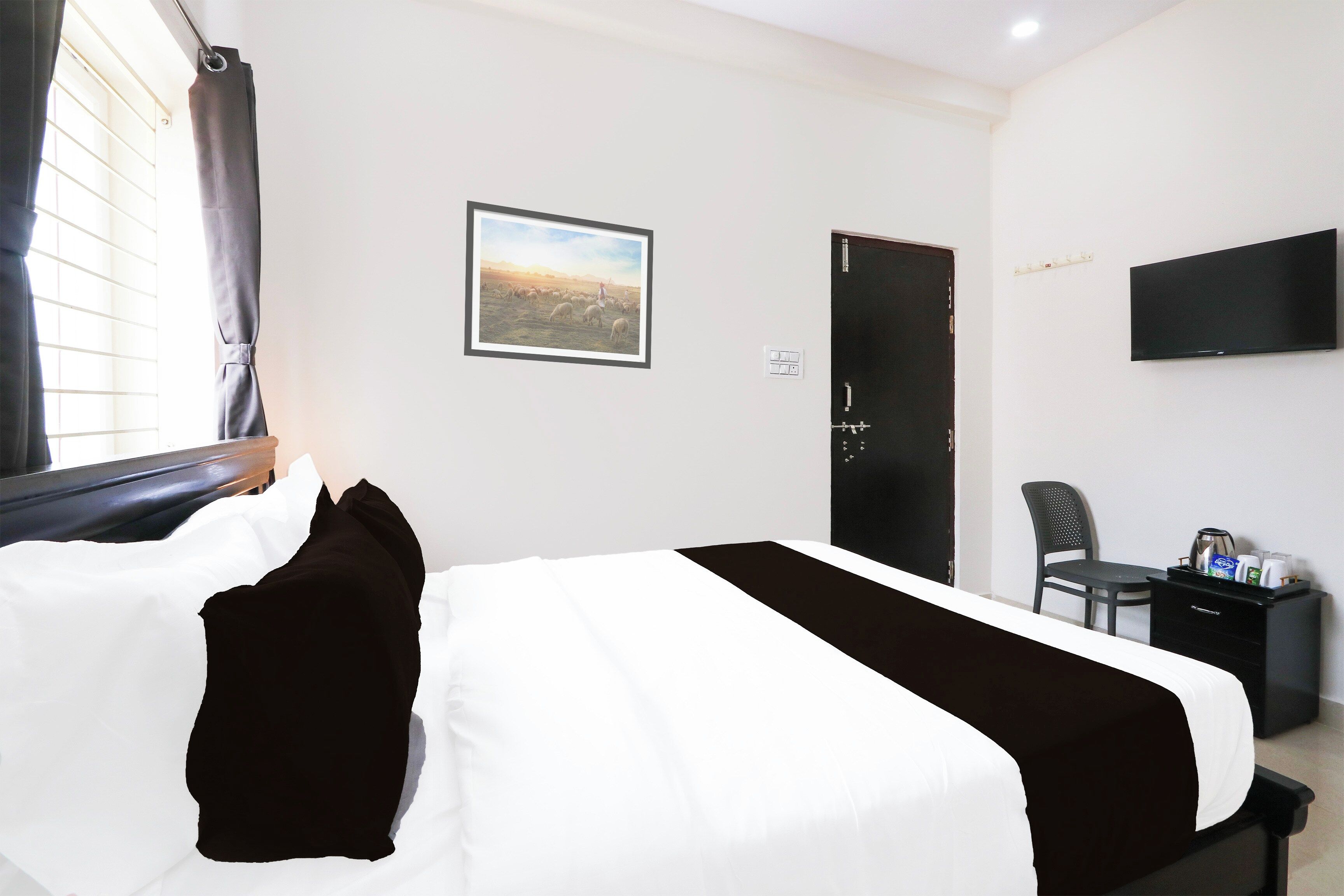 A hotel room with a bed, a flat-screen TV, a desk with a chair, and a painting on the wall.