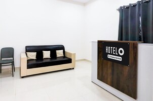 Zona de recepción con un sofá negro y beige, una silla y un mostrador de recepción con un cartel que dice 'HOTEL'.