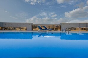 A swimming pool with two lounge chairs and a city skyline in the background. - Kingsgate Hotel Clocktower (Dubai)