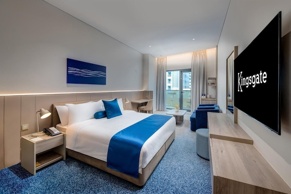A hotel room with a bed, bedside tables, a desk, a chair, a TV, and a window with curtains. - Kingsgate Hotel Clocktower (Dubai)