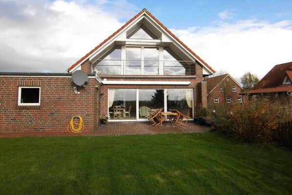 A two-story house with a brick exterior, a large glass door entrance, and a small patio with outdoor furniture. - Holiday home with 2 bedrooms (Jemgum-Ditzum)