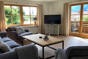A living room with a sofa, a coffee table, a TV, and a sliding glass door leading to an outdoor area. - Holiday apartment with 1 bedroom (Garmisch-Partenkirchen)