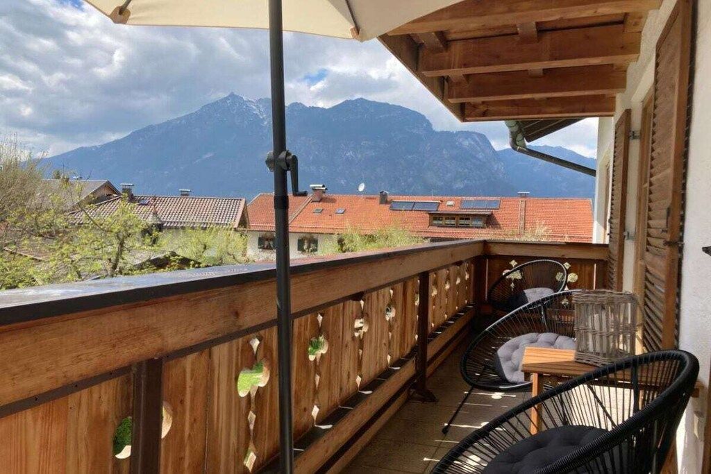 A balcony with a view of mountains, wooden railings, and two black chairs.