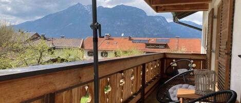 A balcony with a view of mountains, wooden railings, and two black chairs.
