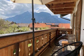 Een balkon met uitzicht op bergen, houten leuningen en twee zwarte stoelen.