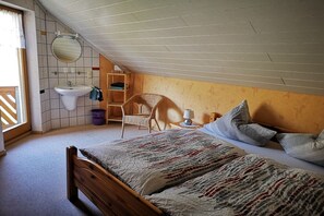 Un dormitorio con una cama de madera, una mesita de noche con lámpara, una silla, un estante pequeño y una ventana con cortinas.