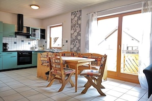 A kitchen with a dining table and chairs, a stove, and a window with curtains. - Holiday apartment with 1 bedroom (Bruttig-Fankel)