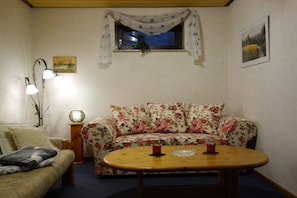 A cozy living room with a floral sofa, a wooden coffee table, and a small window with curtains. - Holiday apartment with 2 bedrooms (Ludwigswinkel)
