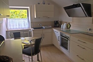 A compact kitchen with a window, a sink, a stove, and a dining area with a chair. - Holiday apartment with 2 bedrooms (Geinsheim)