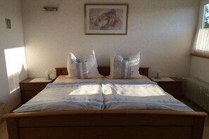 A double bed with a floral bedspread, two bedside tables with lamps, a framed artwork on the wall, and a window with curtains. - Holiday apartment with 2 bedrooms (Geinsheim)
