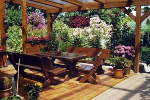 An outdoor patio with a wooden table and benches, surrounded by potted plants and flowers. - Holiday apartment with 2 bedrooms (Geinsheim)